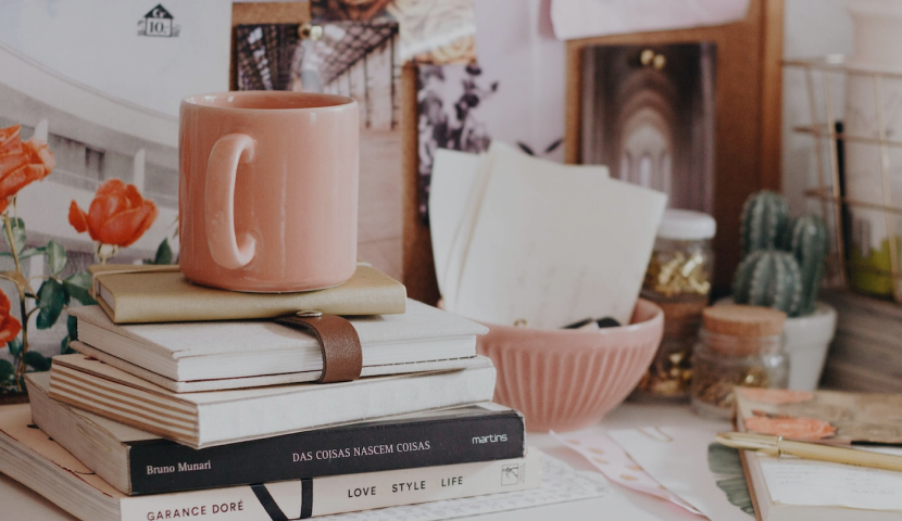 desk with stack of books and pink coffee mug and bowl